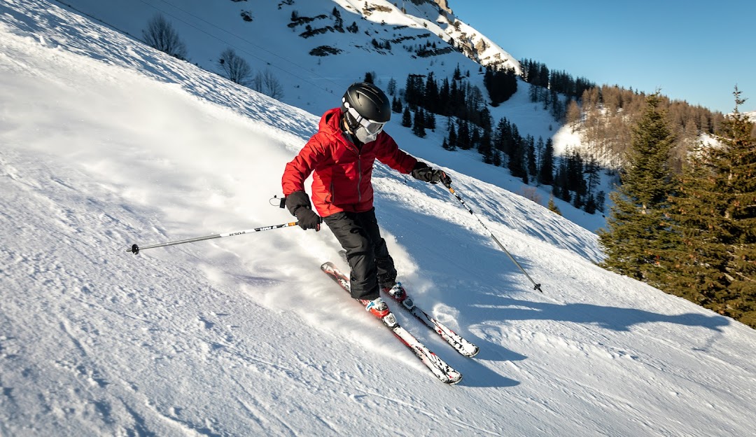 A skier and a snowboarder enjoy a beautiful winter day at the Gresse en Vercors ski resort in Grenoble, France, with children learning to ski in the background.