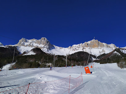 Winter sports scene at Gresse en Vercors ski resort in Grenoble, France. Visible are a ski lift, chalet, and sports centre amidst a snowy landscape.