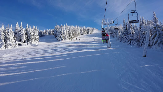 Ski lift at Bonera Ski areál Ramzová, amidst a beautiful winter sports scene at the ski resort. Skiers are enjoying the snowy slopes while a charming challet stands in the distance.