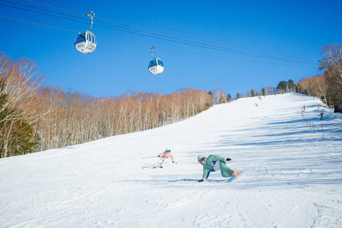 Hunter Mountain Shiobara in Japan - two people skiing down a hill on a sunny day.