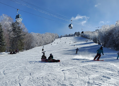 Winter scene at Hunter Mountain Shiobara in Japan with a bustling ski resort. Skiers enjoying the snow-covered slopes, skimming downhill past a ski lift.