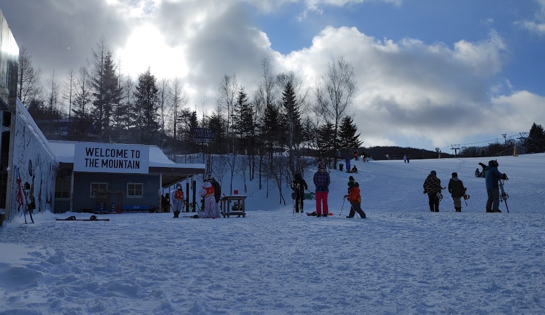 View of a bustling winter sports scene at Hunter Mountain Shiobara in Japan, with various skiers and snowboarders on the slopes and a chalet in the background amidst beautiful snowy landscape.