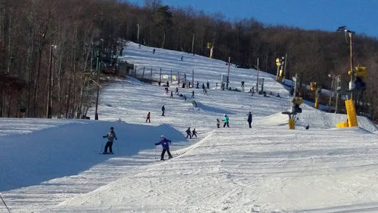 Winter sports scene at Whitetail Ski Resort in Mercersburg, Pennsylvania, featuring a skier and a group of people skiing. A ski lift is also visible in the background.