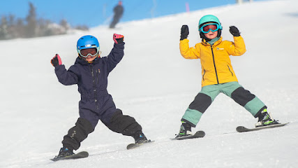 A bustling winter sports scene at Järvsöbacken, Sweden, featuring a skier and a child learning to ski, presumably against the backdrop of a winter sports centre.