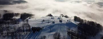 Winter sports scene at Shanty Creek Resorts – Schuss Mountain in Mancelona, Michigan showcasing a ski lift leading to a cozy chalet, with a skier visible on the slopes of the ski resort.