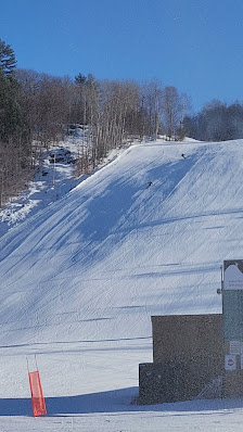A skier is enjoying a winter sports scene at Mont Ste-Marie ski resort in Quebec Canada. They're nearby a ski lift and a snowmobile is also seen enhancing the exhilarating ambiance.