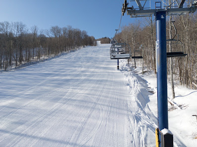 Winter scene at Crabbe Mountain ski resort in Central Hainesville, New Brunswick, Canada with a ski lift visibly transporting skiers to the top of the snowy terrain.