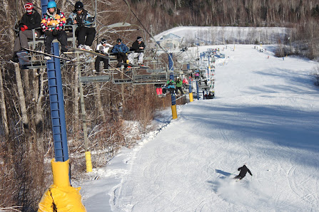 A skier enjoys the winter sports scene at Crabbe Mountain in Central Hainesville, New Brunswick, Canada. The ski lift ascends the snowy slopes of the busy ski resort.