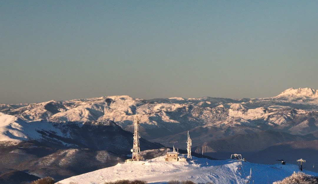 A picturesque winter scene at Vigla Pisoderi ski resort in Verno Greece featuring a rustic chalet amidst snowy slopes populated by enthusiasts enjoying winter sports accentuated by a functioning ski lift.