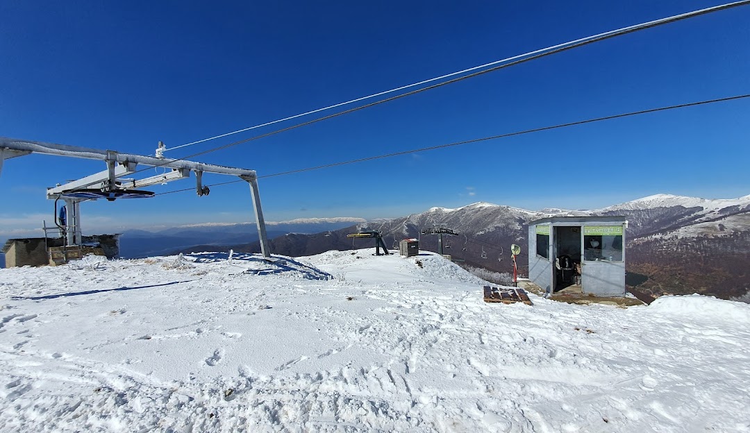 Image showcasing Vigla Pisoderi ski resort in Greece, featuring a ski lift ascending over a snowy landscape, with a skier descending in the fork and a chalet in the distance.