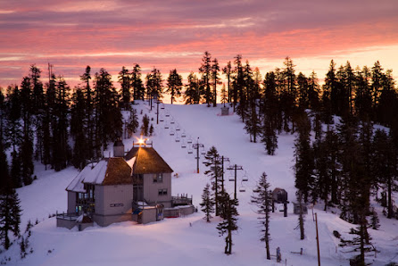 View of Mt. Ashland in Ashland, Oregon showcasing a serene winter setting with a ski resort. Visible features include a ski lift, a mountain hut, and skiers enjoying winter sports.
