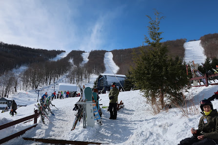 Winter scene at Plattekill in The Catskills, Roxbury, NY featuring a bustling ski resort, a ski lift carrying guests uphill, and skiers gracefully navigating the snowy slopes.