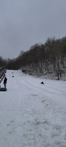 A lively winter sports scene in Plattekill, The Catskills, NY, featuring a snowmobile and a skier amidst a snow-covered ski resort.
