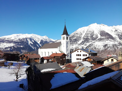 Sunny day at Sportbahnen Eischoll Augstbordregion in Switzerland. A winter sports scene is highlighted by a picturesque chalet and towering mountain in the background.