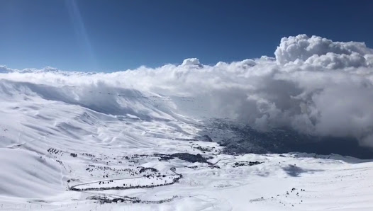 A winter scene overlooking snowy Cedars Bsharri in North Lebanon featuring a ski resort settled in the heart of the mountains. Skiers are seen enjoying their winter sports activities.