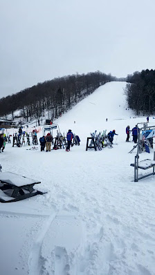 A winter sports scene at Song Mountain Finger Lakes. Skiers navigate snowy slopes beneath a ski lift reaching towards the chalet. Ski resort vibes in Tully New York.
