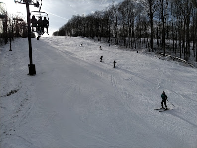 A skier glides down a snowy slope at Song Mountain ski resort in Tully New York with the ski lift and chalet visible in the background embodying a bustling winter sports scene.