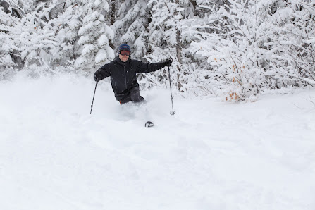 A skier in action at Black Mountain of Maine, enjoying a bright winter day on the snow-covered slopes of this popular ski resort. The festive winter sports scene is energy-filled and vibrant.