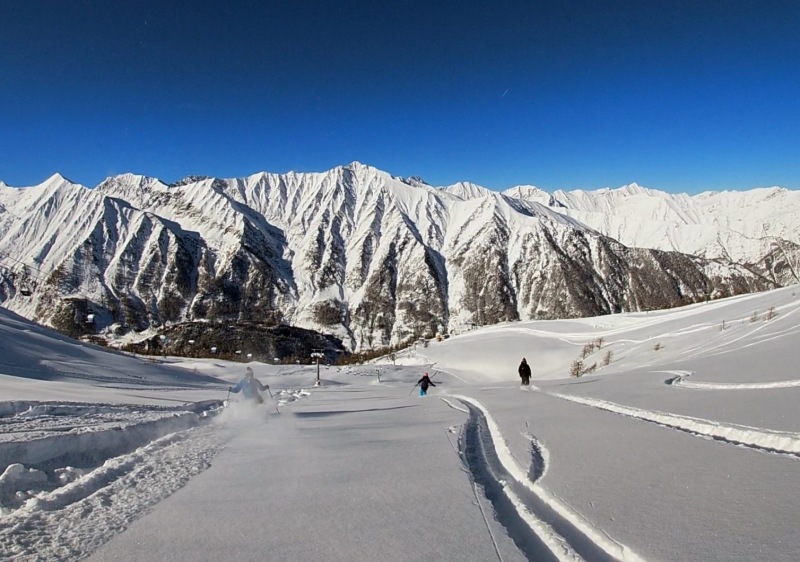 Winter sports enthusiasts enjoying a day at the Prali ski resort in Turin, Italy, against a stunning backdrop of snow-covered mountains.