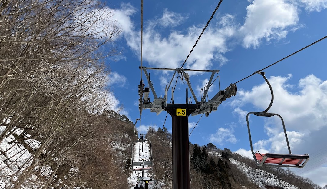 Ski lift ascending a snow-covered mountain at a ski resort in Tainai, Chūbu, Japan. A skier and a chalet can be barely seen amidst the winter sports scene.