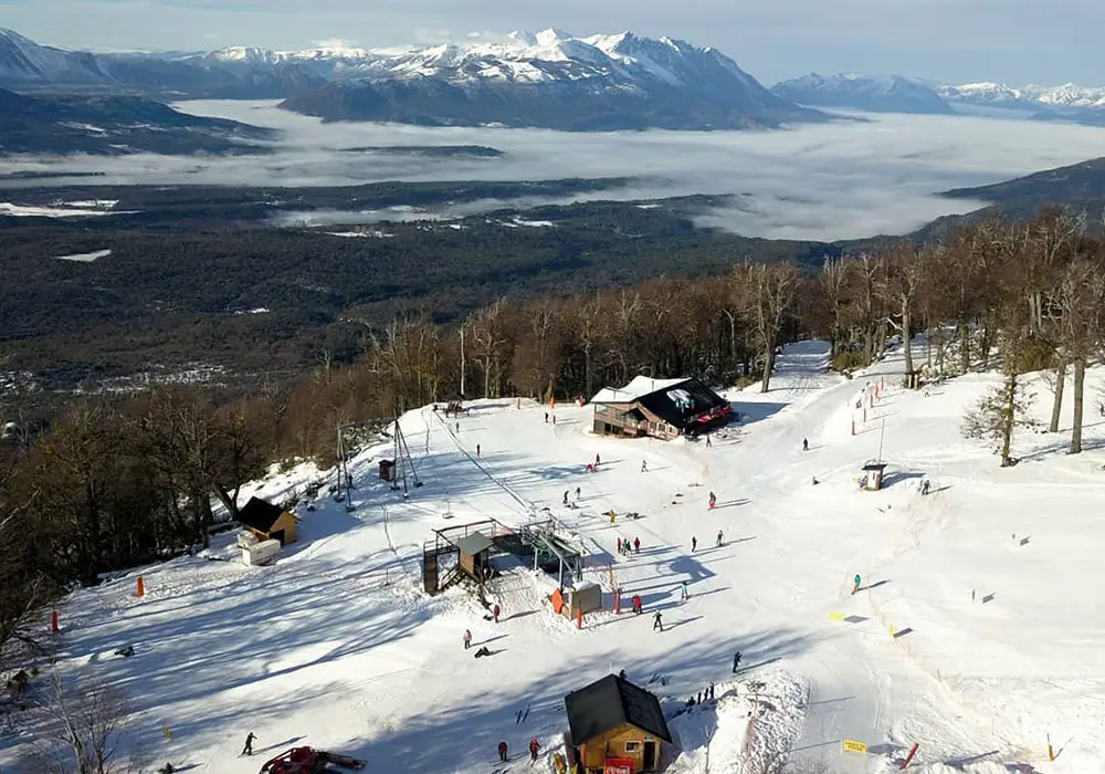 A winter sports scene at Cerro Perito Moreno ski resort in El Bolsón, Argentina, featuring a chalet nestled in stunning winter scenery.