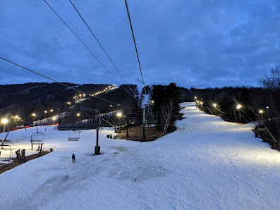 View of Jiminy Peak ski resort in Massachusetts, featuring a ski lift carrying visitors up the snow-covered slopes. Winter sports enthusiasts can be seen enjoying activities in the chill.
