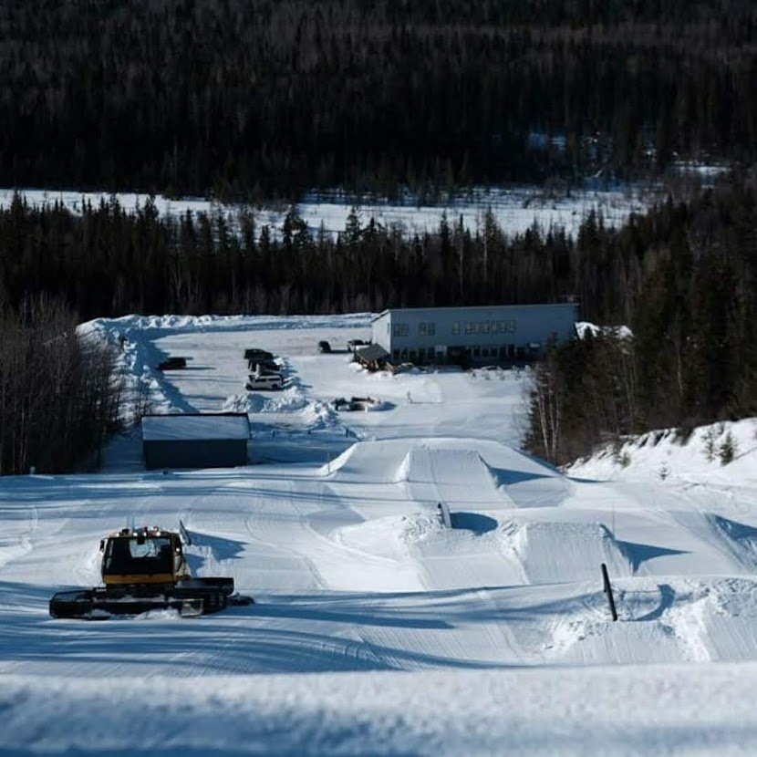 Winter sports scene at Murray Ridge in Fort St James, British Columbia showcasing a bustling ski resort surrounded by pristine snow, a distant skier, and a parked snowmobile.