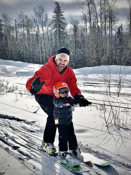 A snowboarder skillfully rides down Murray Ridge in Fort St James, British Columbia, Canada, carving through fresh, powdery snow under a vibrant blue sky.