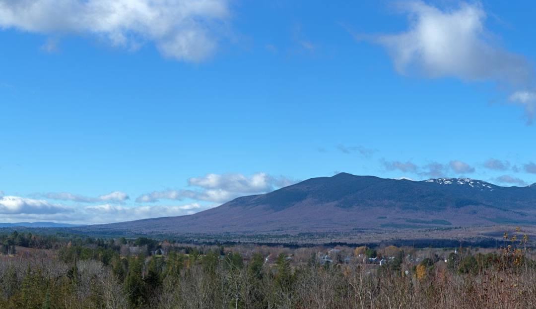 A view of Mt Abram in Greenwood Maine with a beautiful sunny sky above. There's a quaint chalet nestled on its snowy slopes. Winter sports enthusiasts populate the scene dotting the landscape.