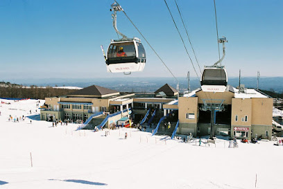 A scenic view of Mt. Jeans Nasu ski resort in Japan during winter featuring a ski lift moving through the snow-covered landscape with a skier in the distance enjoying the slopes.