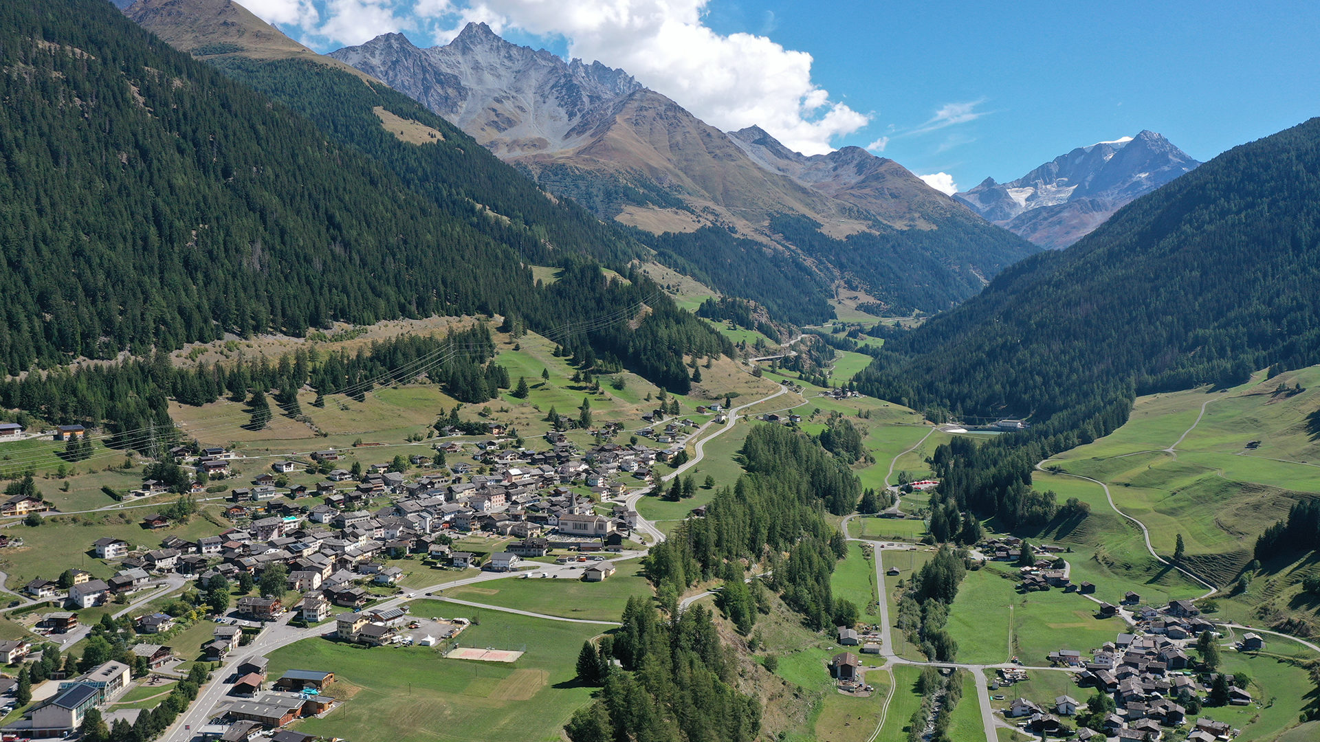 Image of a cheerful chalet nestled in Vichères, Switzerland. The ski resort in the backdrop along with a towering mountain and clear sunny skies capture Switzerland's serene winter scene.