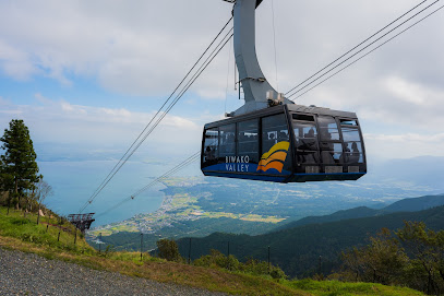 A ski lift traversing the snowy slopes of Biwako Valley in Kansai Japan with a challet and large mountain looming in the distance. A lone skier is visible adding to the charm of the ski resort.
