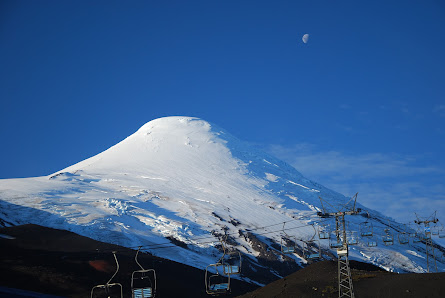 A picturesque view of Osorno in Puerto Varas Chile accentuated by the magnificent snowy mountain in the background. Close by a charming challet sits nestled possibly part of a ski resort offering winter sports activities.