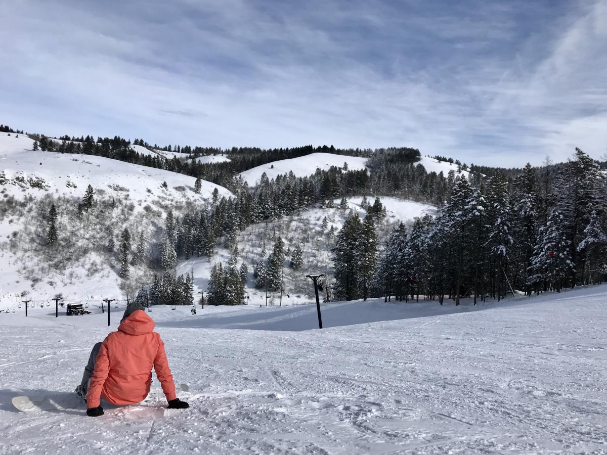 Kelly Canyon in USA - a person sitting on the snow in front of a mountain.