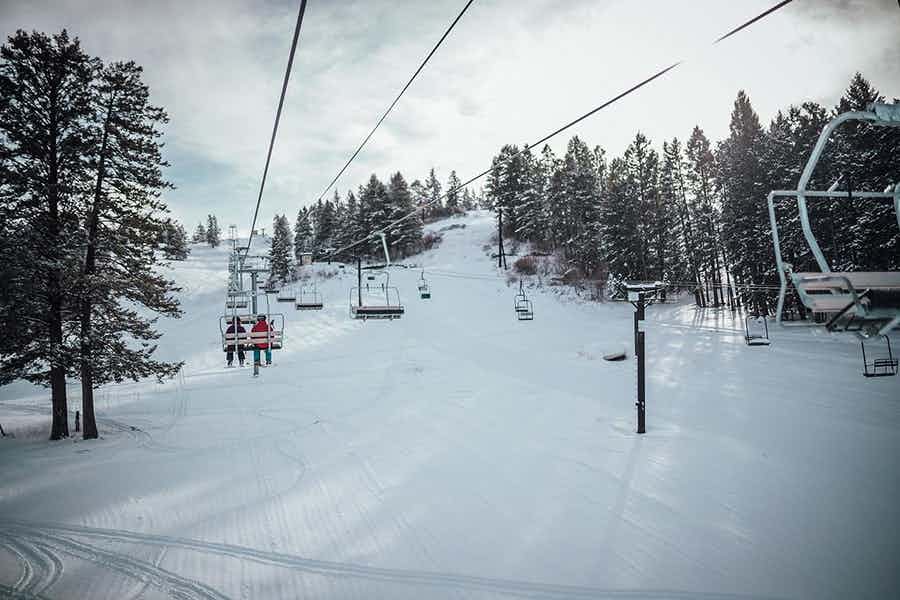 A winter scene at Kelly Canyon Ski Resort in Ririe Idaho showcasing a ski lift on snowy slopes filled with people enjoying winter sports activities like skiing.