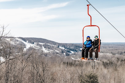 Image shows a ski lift at Jackson Creek Summit in Wakefield Michigan amidst a winter landscape. A skier can be faintly noticed in this snowy ski resort scene.