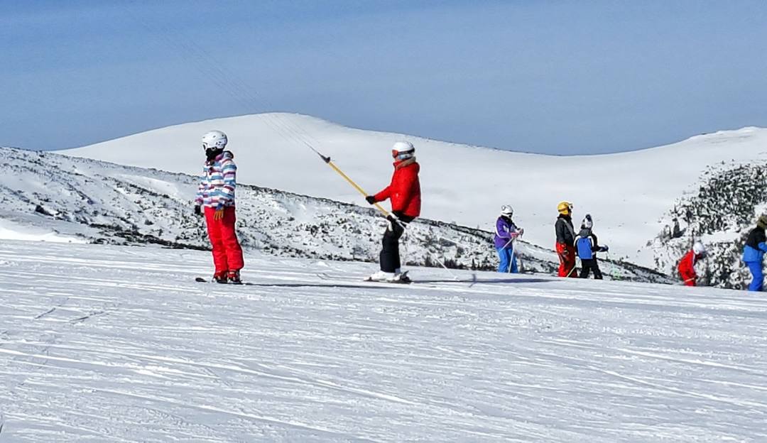 A winter sports scene in Transalpina Romania featuring a skier and a group of people enjoying skiing activities at a winter sports centre.