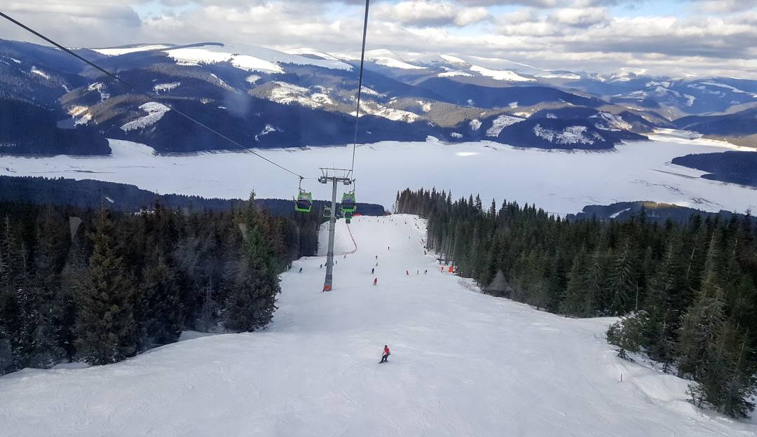 View of Transalpina ski resort in Romania featuring a ski lift a skier enjoying the snow-covered slopes and a bustling winter sports scene.