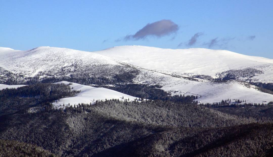 View of Transalpina-Vidra Voineasa in Obârșia Lotrului, Romania featuring a mountain with snow-covered slopes, a challet, part of the ski resort, and winter sports activity.