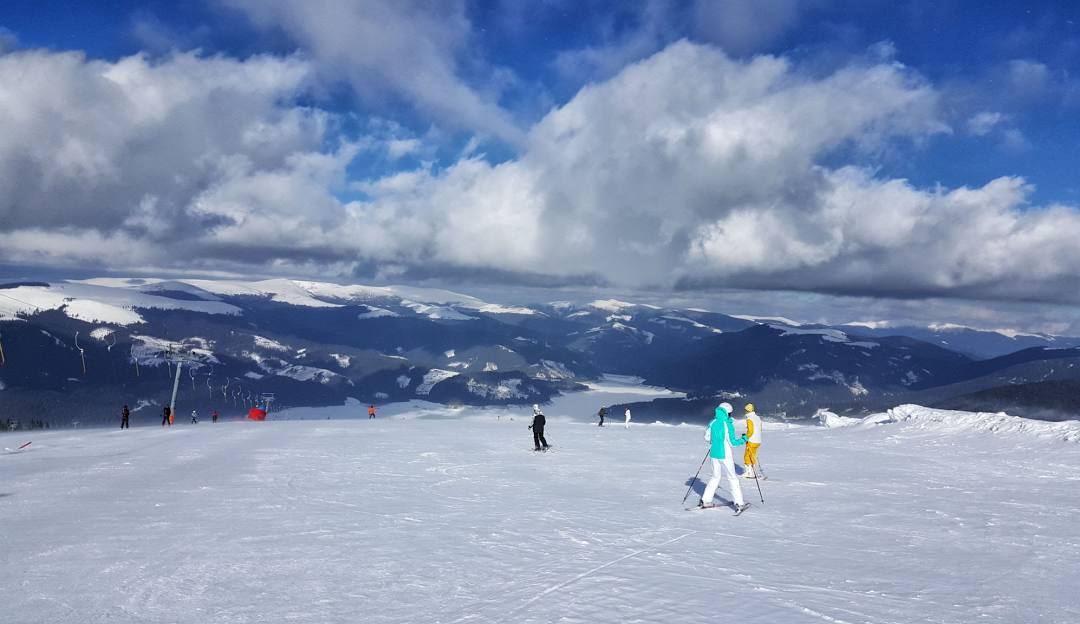 Skiers enjoying a day on the slopes at the Transalpina Ski Resort in Vâlcea, Romania, with a charming challet visible in the background.