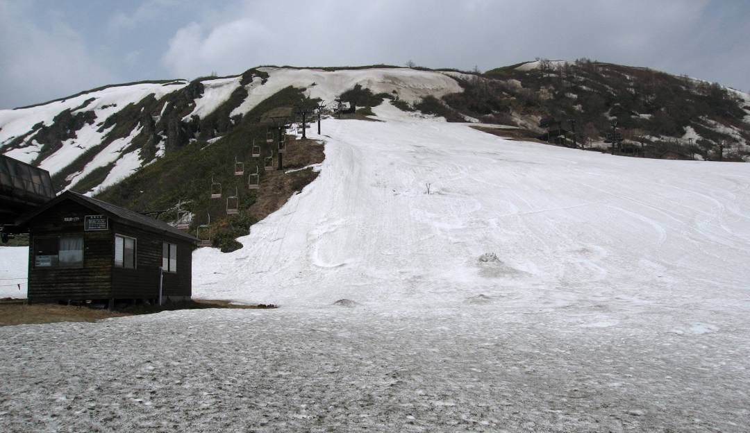 A ski lift ascends a mountain at Kusatsu Onsen ski resort in Japan, showcasing a lively winter sports scene. A charming chalet adds to the scenic beauty of this winter wonderland.