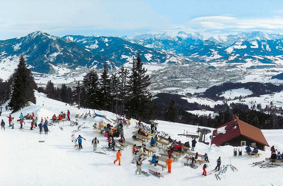 View of Mittagbahn ski resort in Immenstadt, Germany, featuring a ski lift, chalet, and winter sports enthusiasts enjoying the snow-covered, scenic alpine landscape.