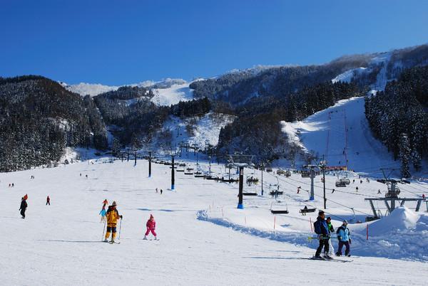 Winter scene at Tateyama Sanroku Raicho Valley Area, Japan, featuring a ski resort with active sportsmen and a chalet amidst stunning snowy scenery.