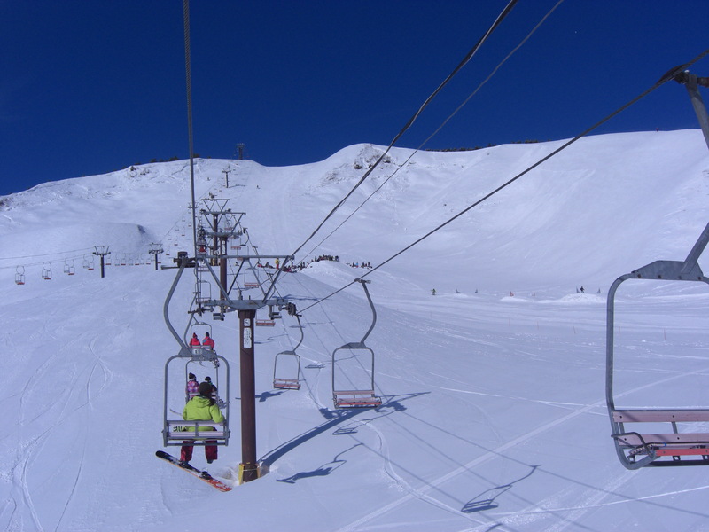 Winter scene at Hyper Bowl Tohachi ski resort in Japan, featuring a chalet nestled in a snowy landscape, ski lift in the background, and a skier navigating the mountainous terrain.