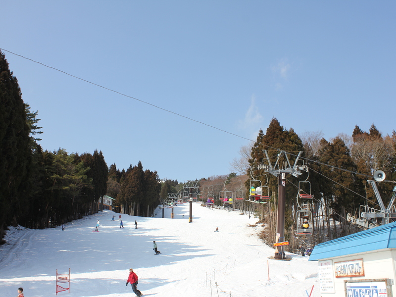 A picturesque view of Hyper Bowl Tohachi a ski resort in Japan displaying a bustling winter sports scene with a ski lift traversing the snowy terrain.