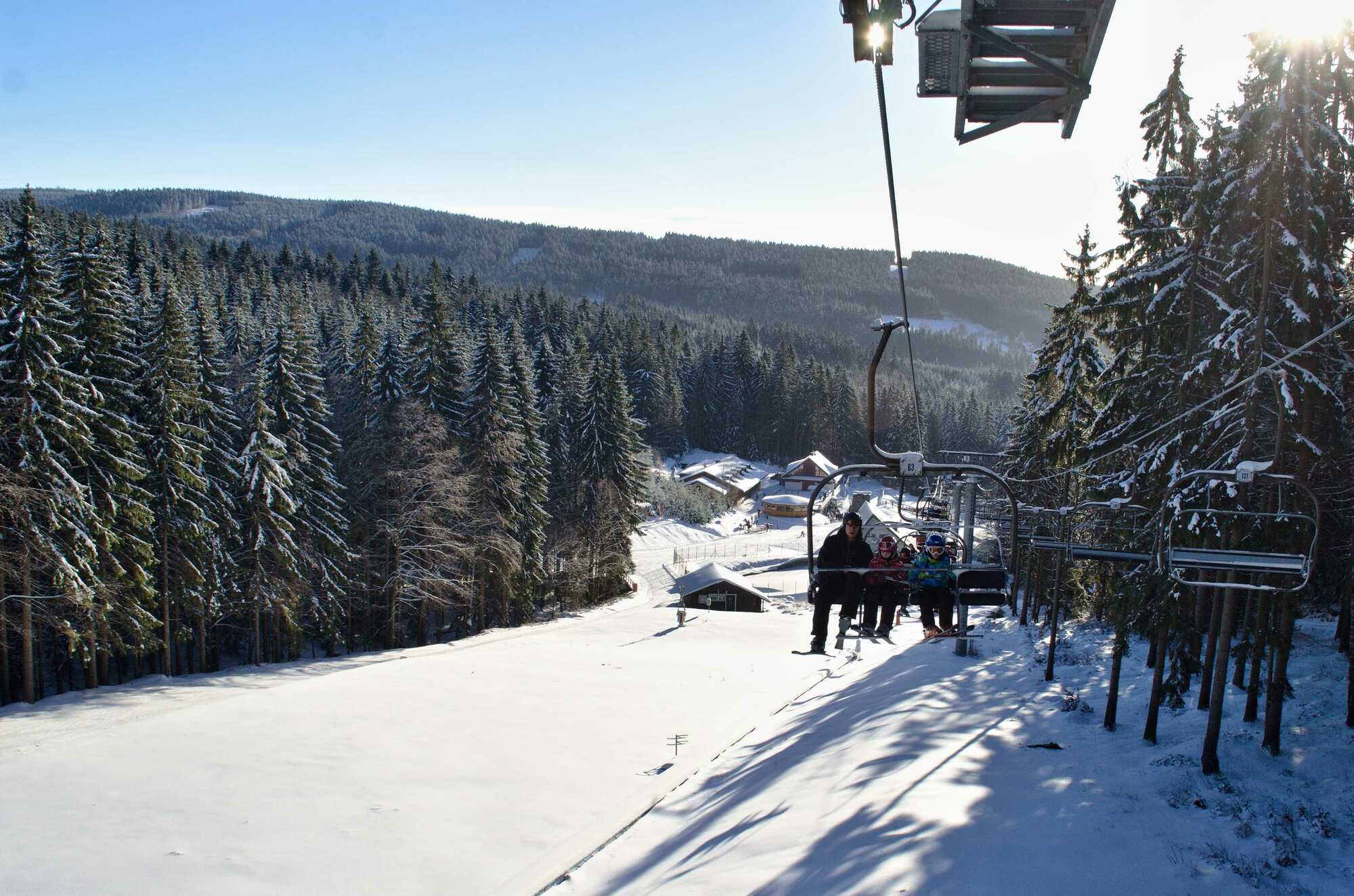 A lively scene at the Ski center Říčky in Czech Republic, showcasing a bustling ski resort with a view of a ski lift, surrounded by a winter sports scene against the backdrop of a charming challet.