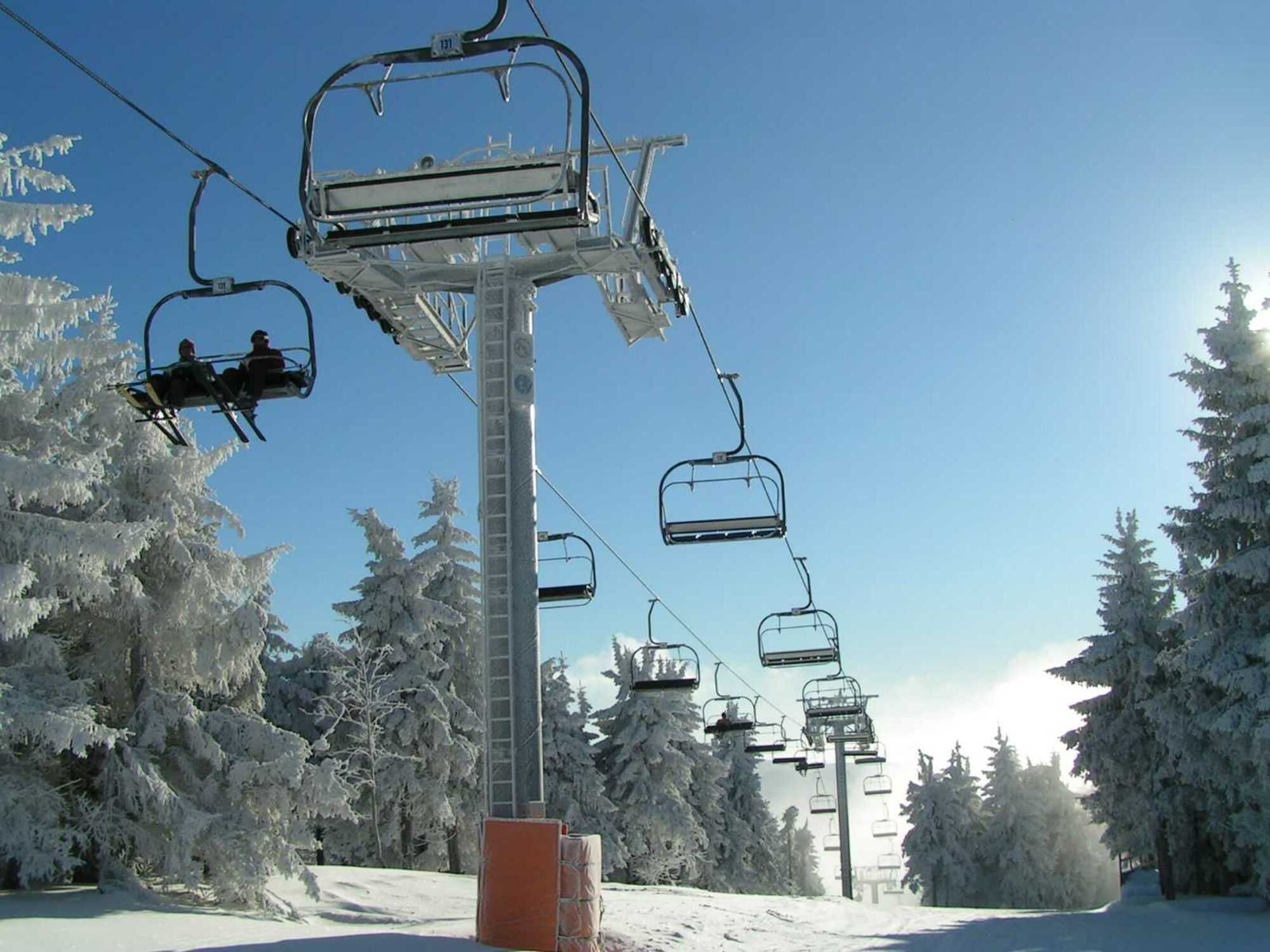 Ski lift ascending a snowy slope at Říčky Ski center, Czech Republic, with a chalet nestled among pines. Winter sports enthusiasts enjoying the ski resort under the clear sky.