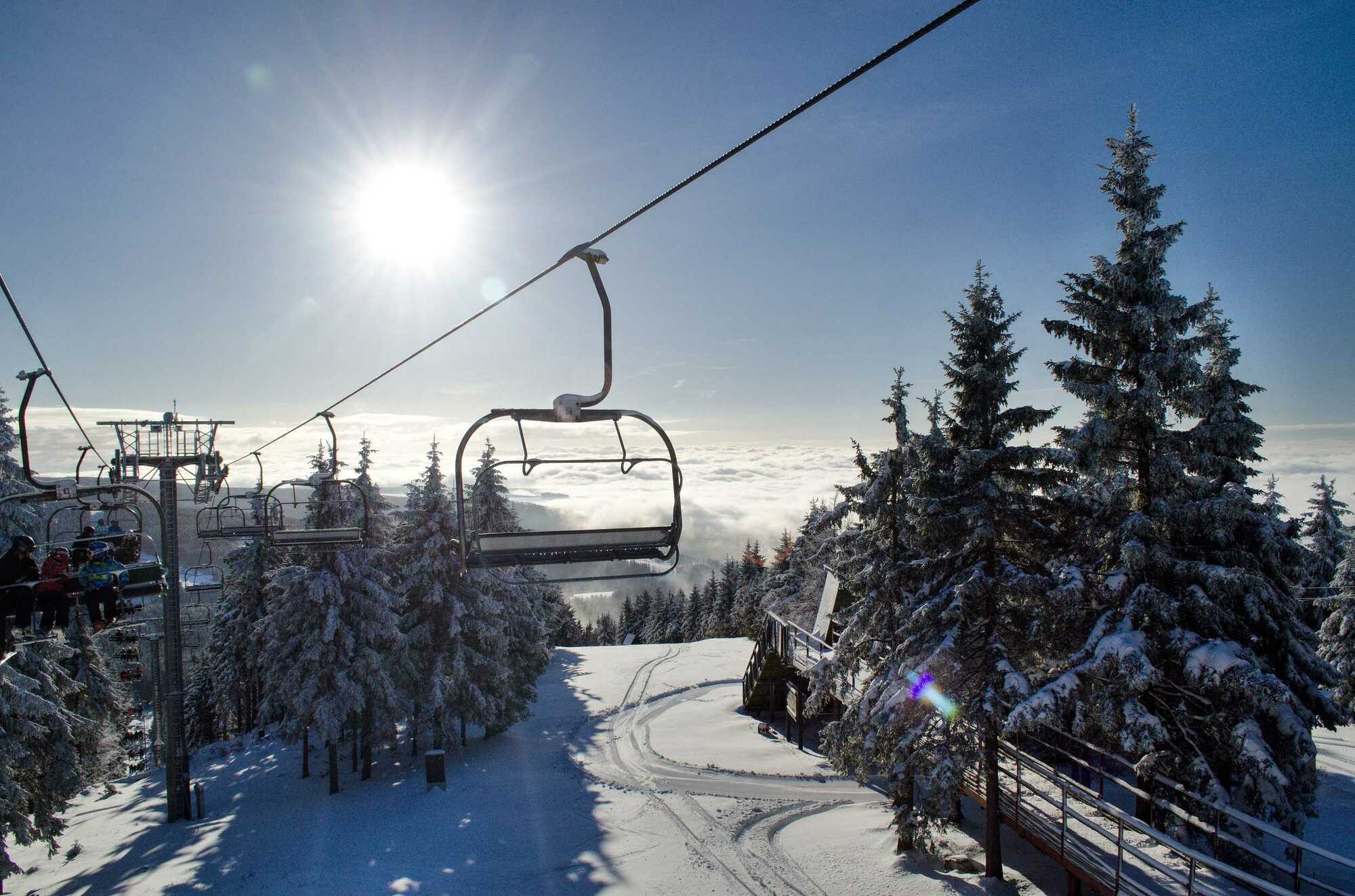 Ski scene at Říčky Ski Center in Czech Republic featuring a ski lift traversing the snowy terrain, a bustling ski resort, skiers on the slopes, and a chalet nestled in the distance.