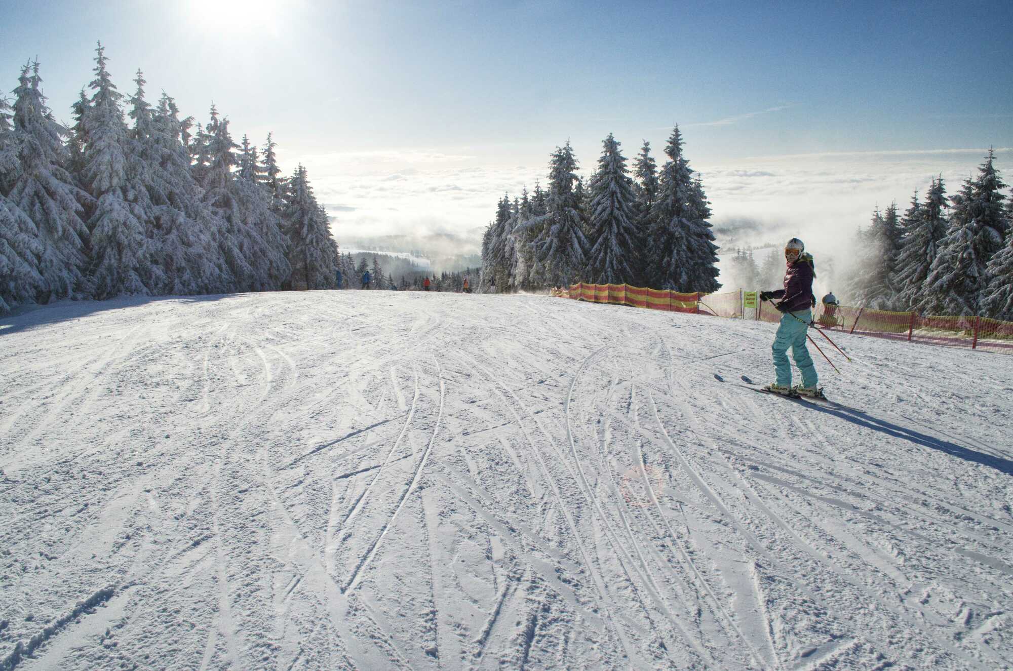 A skier is descending a slope at the Říčky Ski Center in the Czech Republic surrounded by snow-covered landscapes. The ski lift in the background connects the various parts of the winter sports resort.