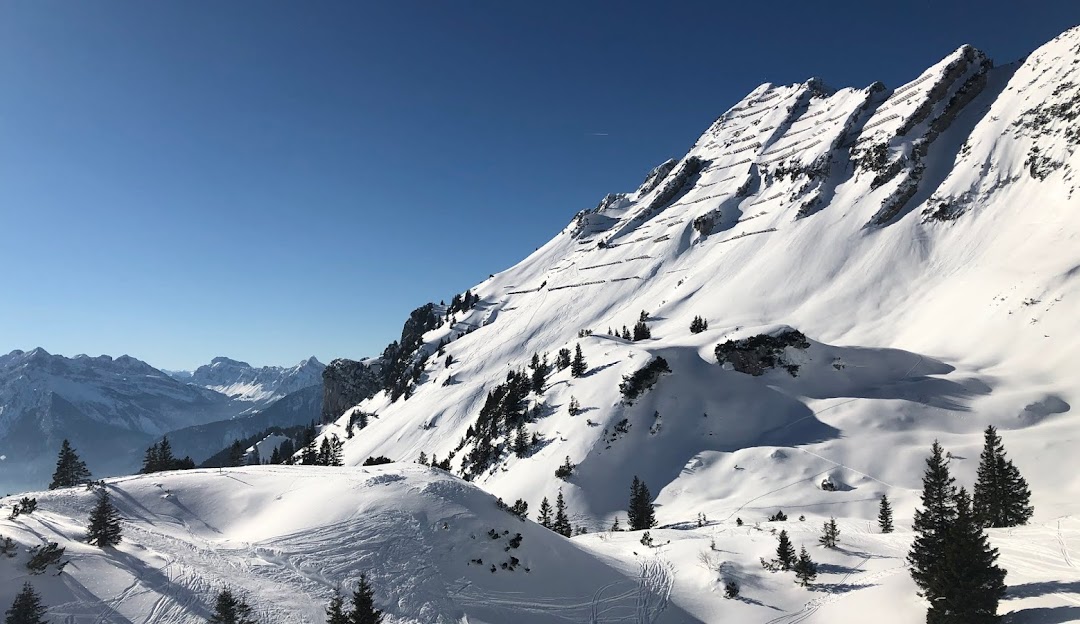 View of the Sesselbahn Mattstock ski resort in Amden, Eastern Switzerland features snow-covered slopes for winter sports, a classic Swiss chalet, and majestic mountains.